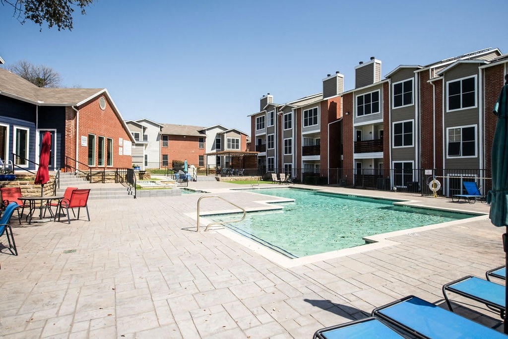 A large swimming pool surrounded by a brick patio and chairs.