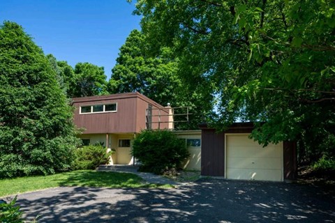 A house with a brown garage door is surrounded by green trees.