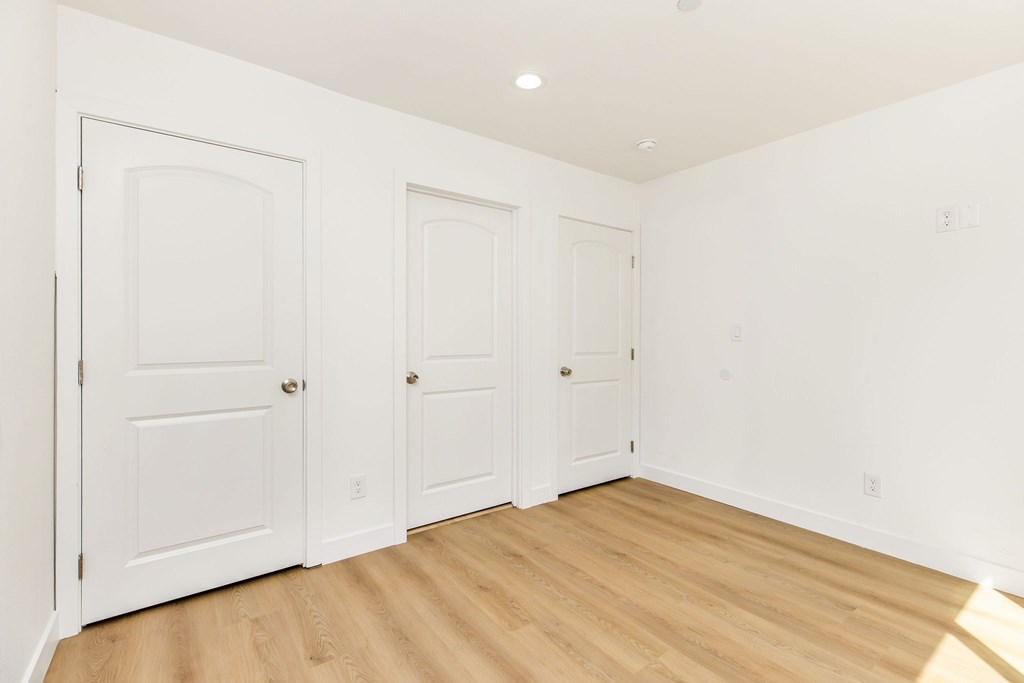 Three white doors in a room with wood floors.