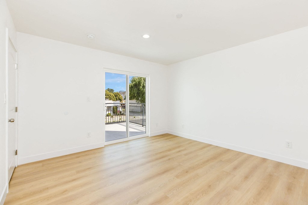 A room with white walls and wooden flooring, leading to a balcony with a railing.