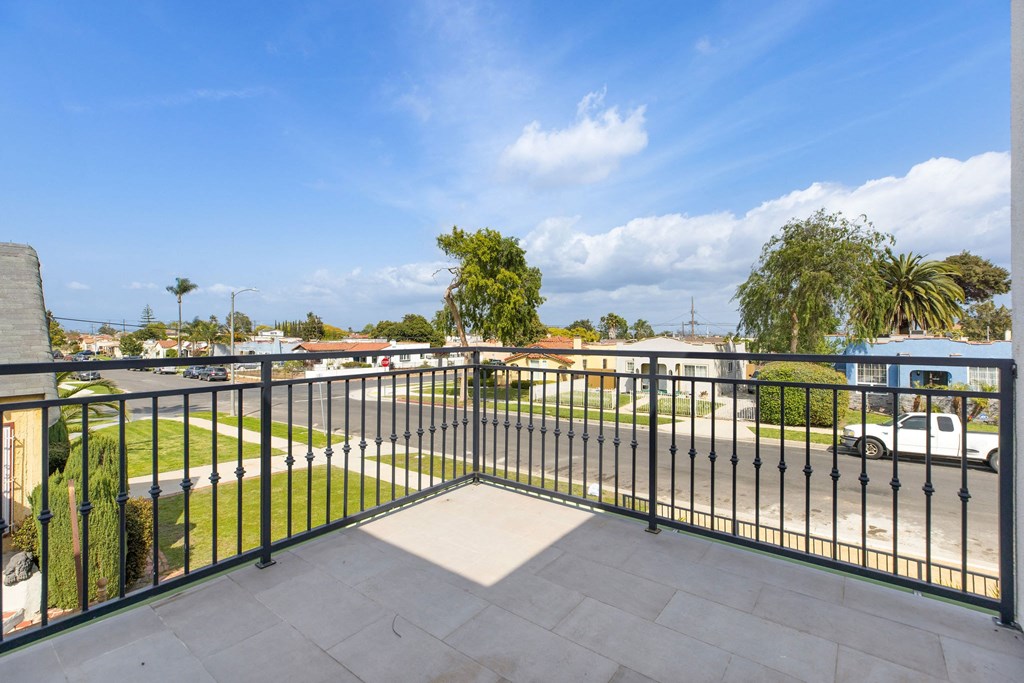 A balcony with a black railing overlooks a residential street.