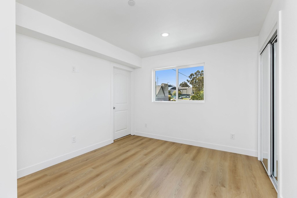 A room with wooden flooring and a window showing a house.