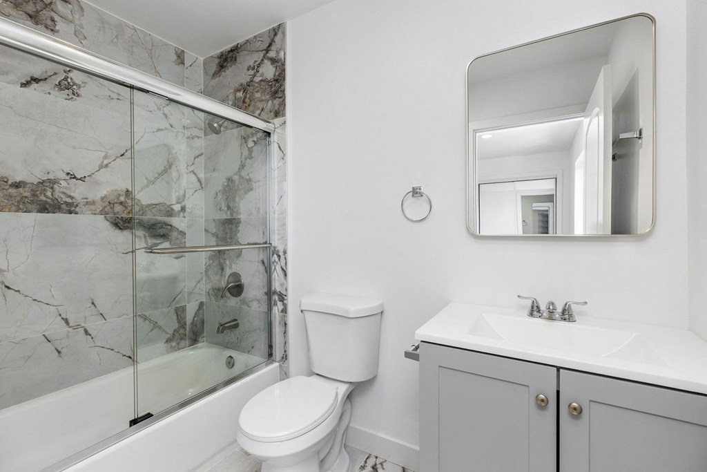 A bathroom with a marble shower, toilet, and sink.