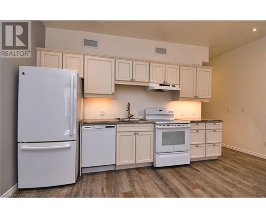 A white refrigerator is in a kitchen with white cabinets and a white stove.