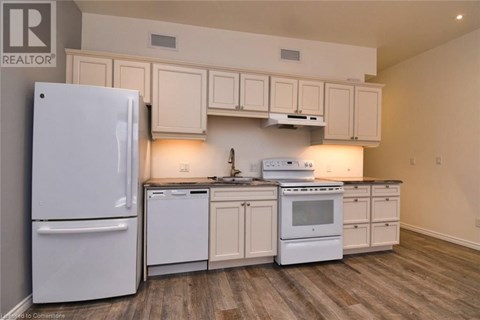 A white refrigerator is in a kitchen with white cabinets and a white stove.