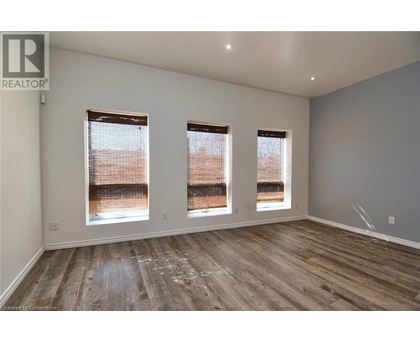 A room with wooden flooring and three windows.