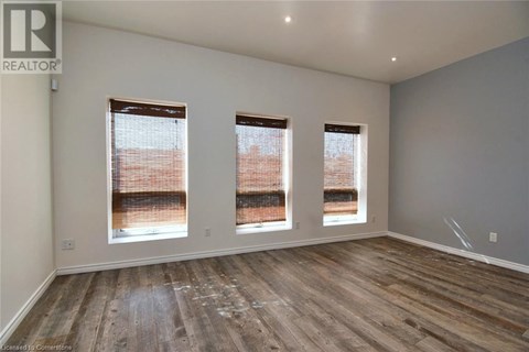 A room with wooden flooring and three windows.