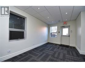 A room with a grey carpet and a white wall with a window and an exit sign.