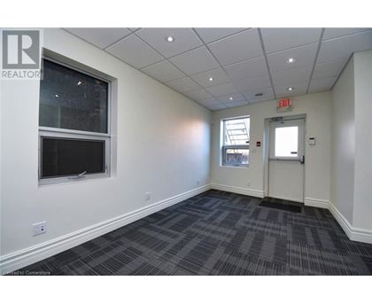A room with a grey carpet and a white wall with a window and an exit sign.