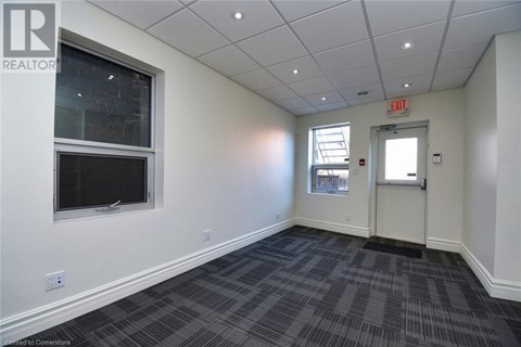A room with a grey carpet and a white wall with a window and an exit sign.