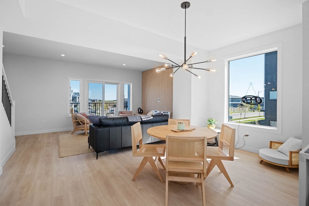 A modern living room with a black sofa, wooden chairs, and a large window.