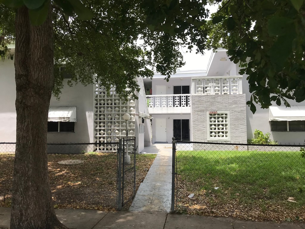 A white building with a black fence and a tree in front.