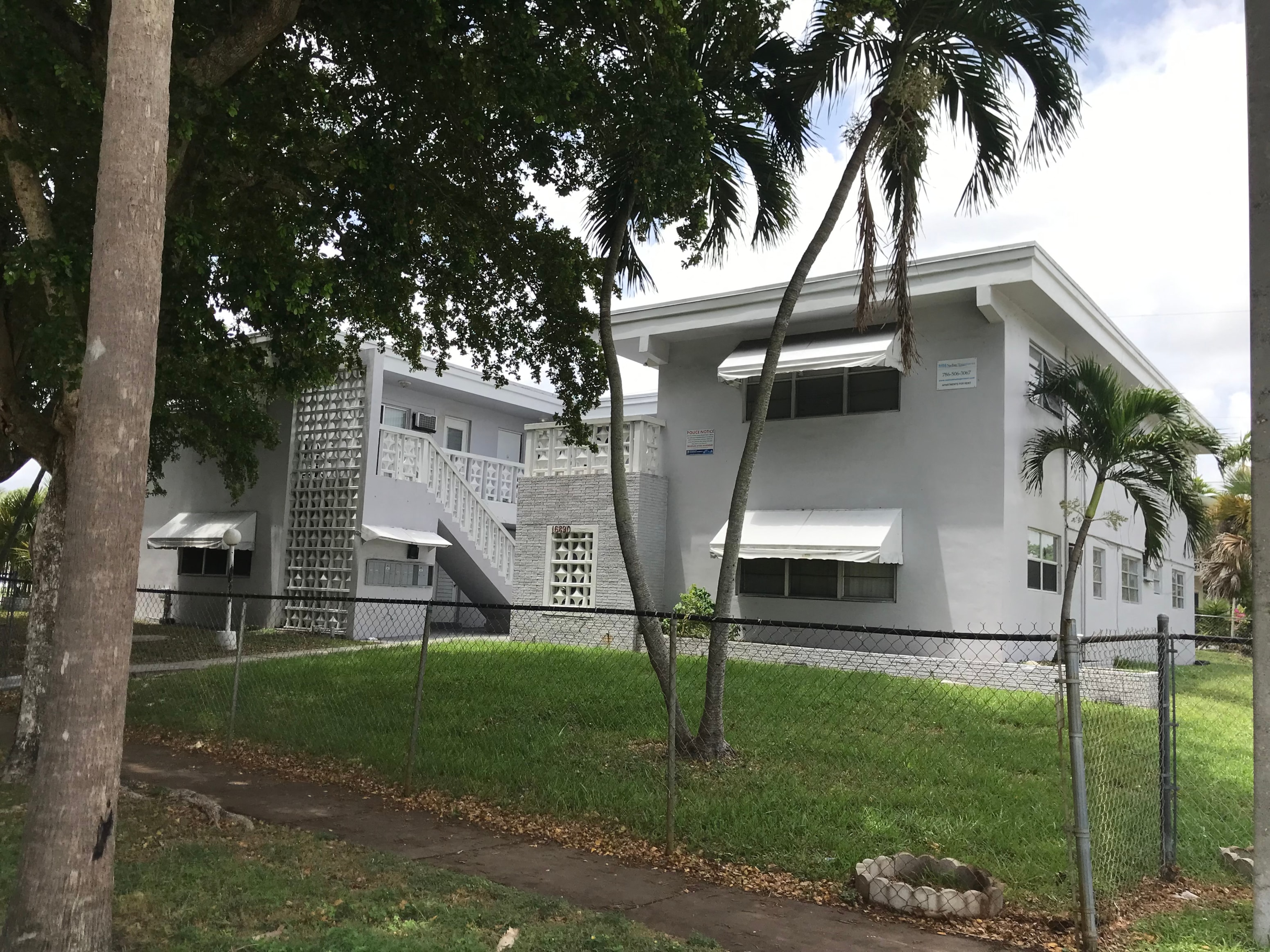 A white building with a black fence and trees in front.