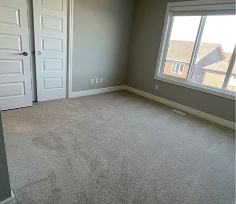 A room with a carpeted floor, a window, and a view of houses outside.