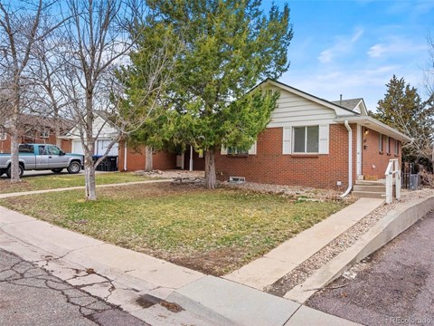 A house with a red brick exterior and a white door is surrounded by a grassy area and a sidewalk.
