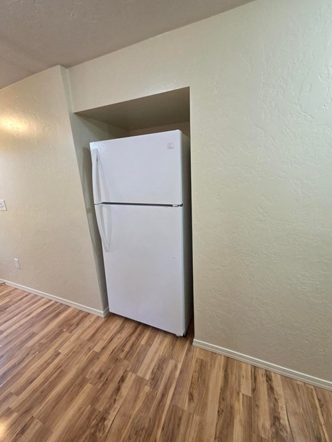 A white refrigerator in a room with wooden flooring.