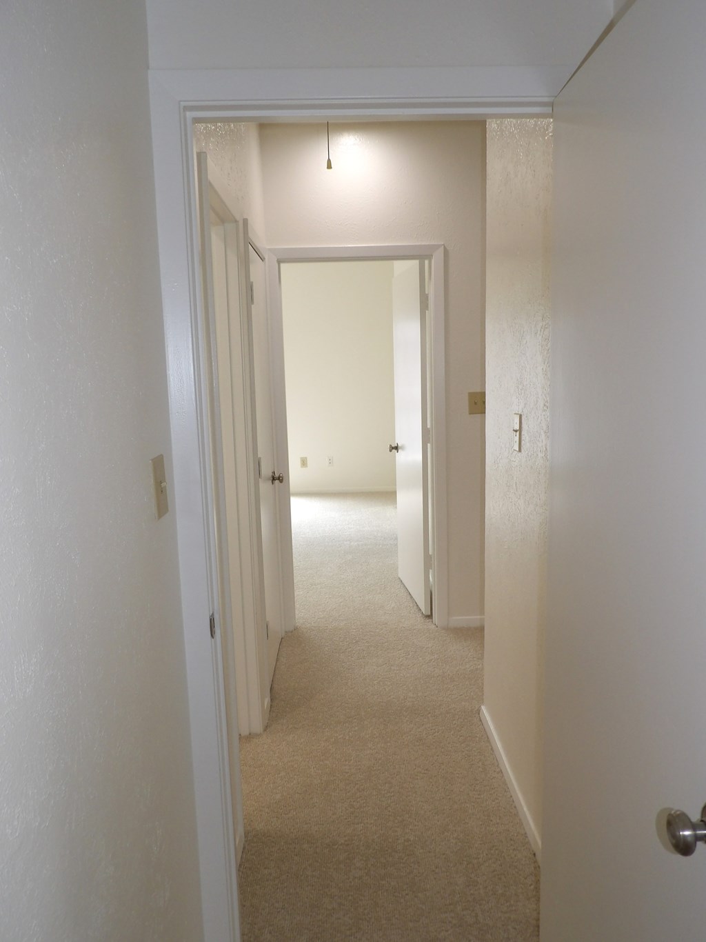 A hallway with a carpeted floor and white walls.