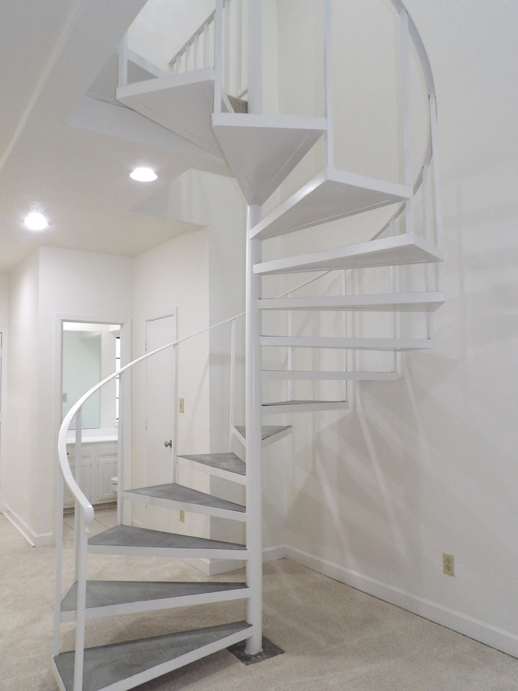 A white spiral staircase with a grey bottom step.
