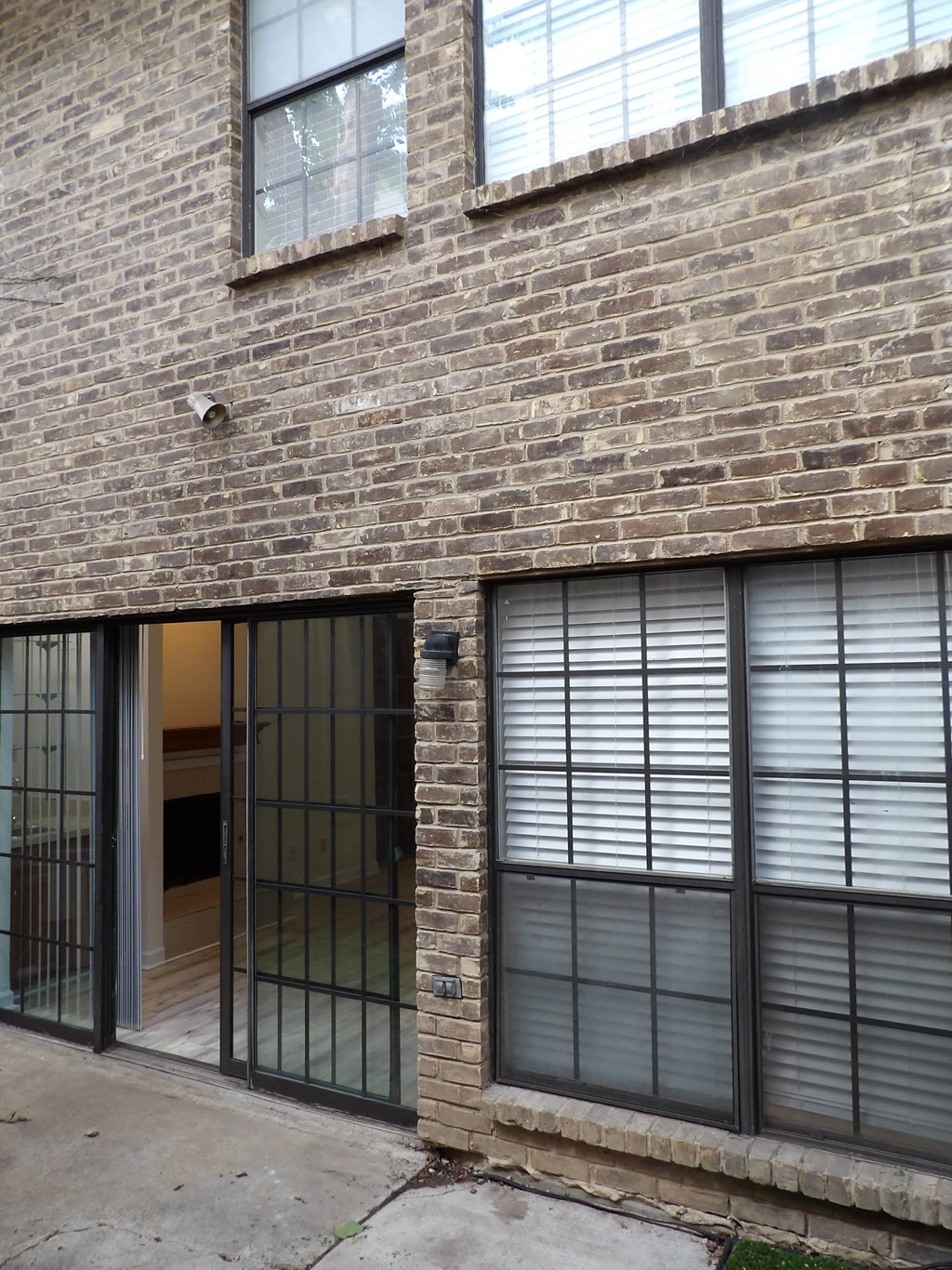 A brick building with a black gate and window with blinds.