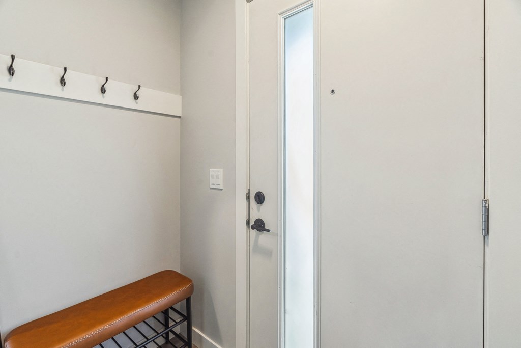 A white door is in a room with a bench and hooks on the wall.