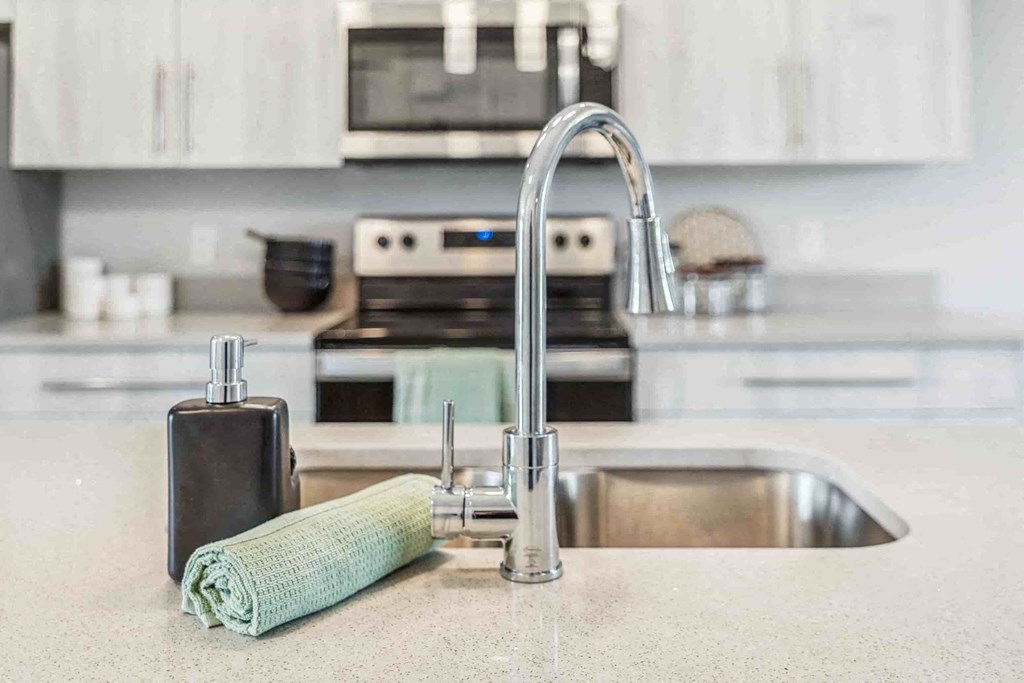 A kitchen sink with a green towel and soap dispenser.