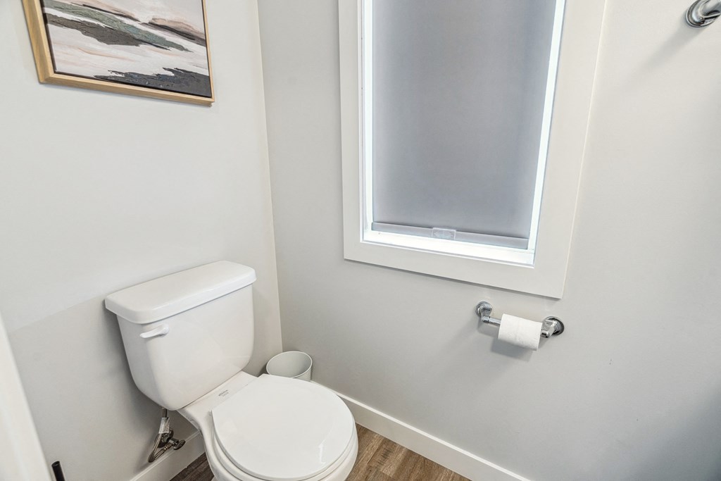 A white toilet with a roll of toilet paper on the wall.