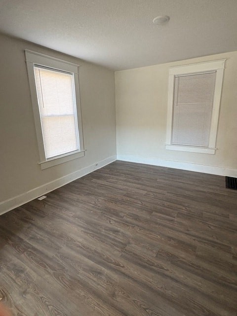 A room with wooden flooring and two windows.