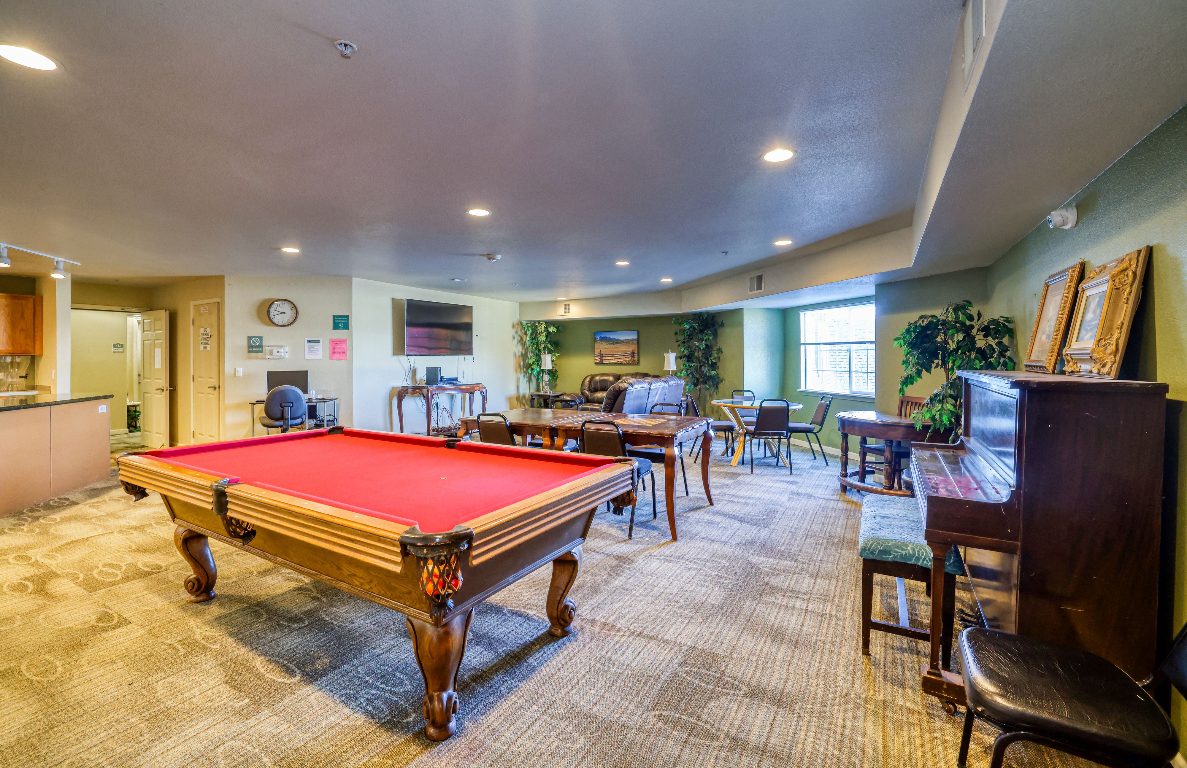 A pool table is in the middle of a room with chairs and a bar.