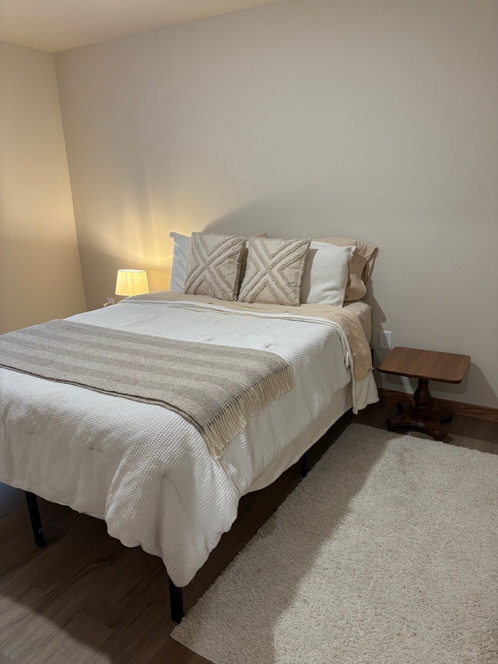 A bed with a white comforter and two pillows with a tan throw blanket on it.
