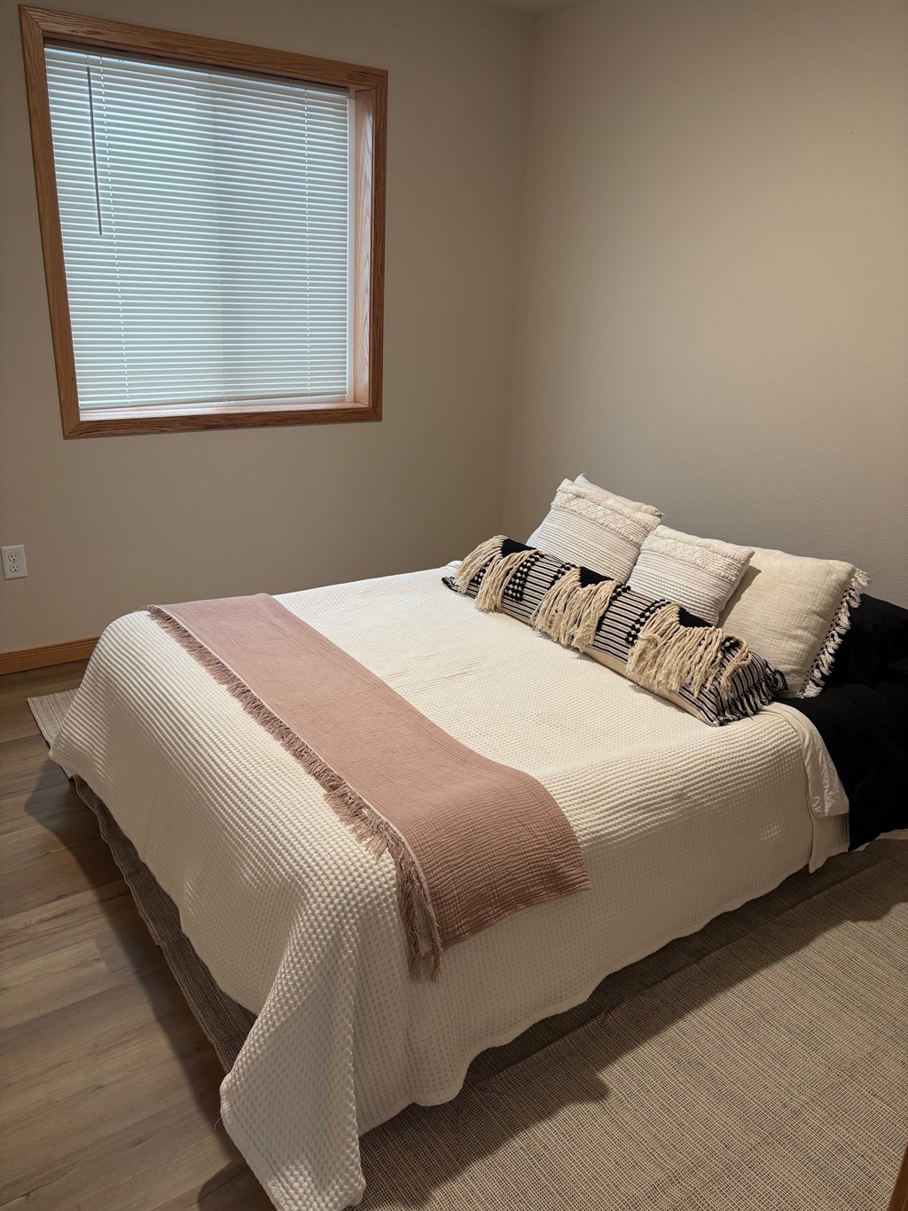 A bed with a white comforter and a pink blanket is in a room with a window.