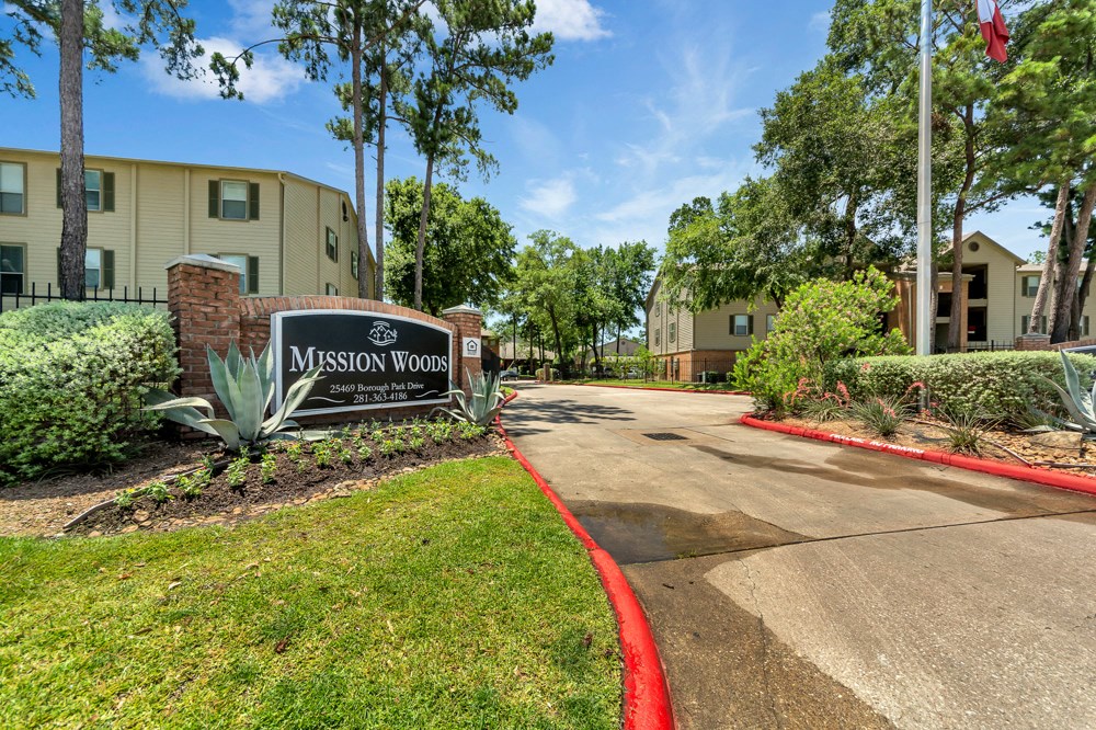 The image shows the entrance to Mission Woods Community with a sign and a flag.