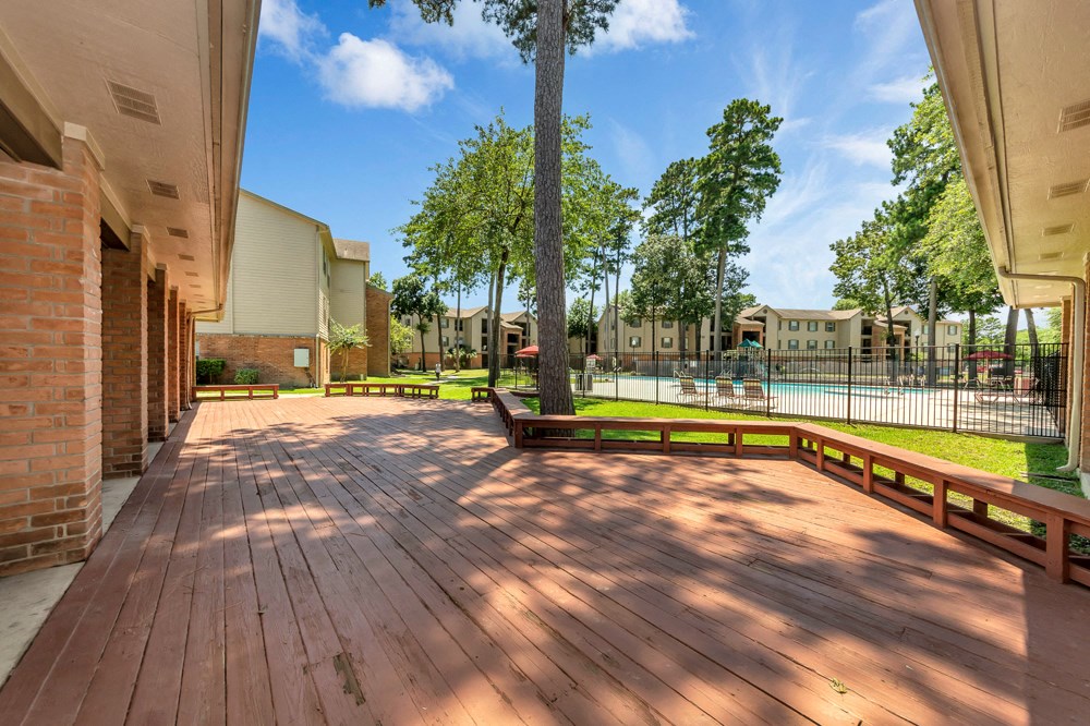 A wooden deck with a bench and a tree in the middle of a sunny day.