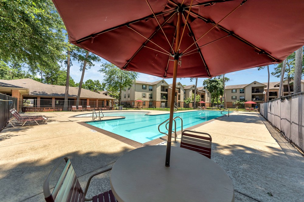 A red umbrella is over a table with a pool in the background.