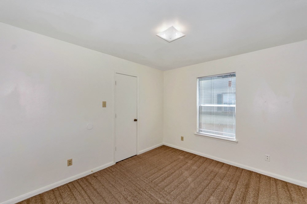 A room with a carpeted floor and a window with blinds.