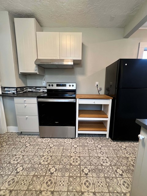 A kitchen with a black fridge and a stove top oven.