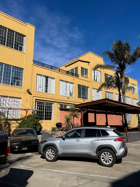 A silver car is parked in a lot in front of a yellow building.