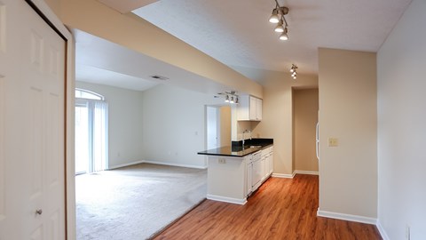 A kitchen with white cabinets and a black countertop is visible from an open doorway.