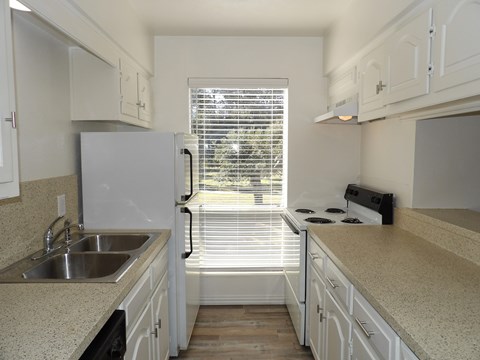 A kitchen with white cabinets and a window with blinds.