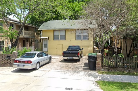 A silver car is parked in front of a yellow house.
