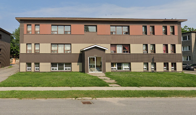 A building with a brown and beige facade has a green lawn in front.