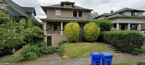 A house with a front yard and two blue bins in front.