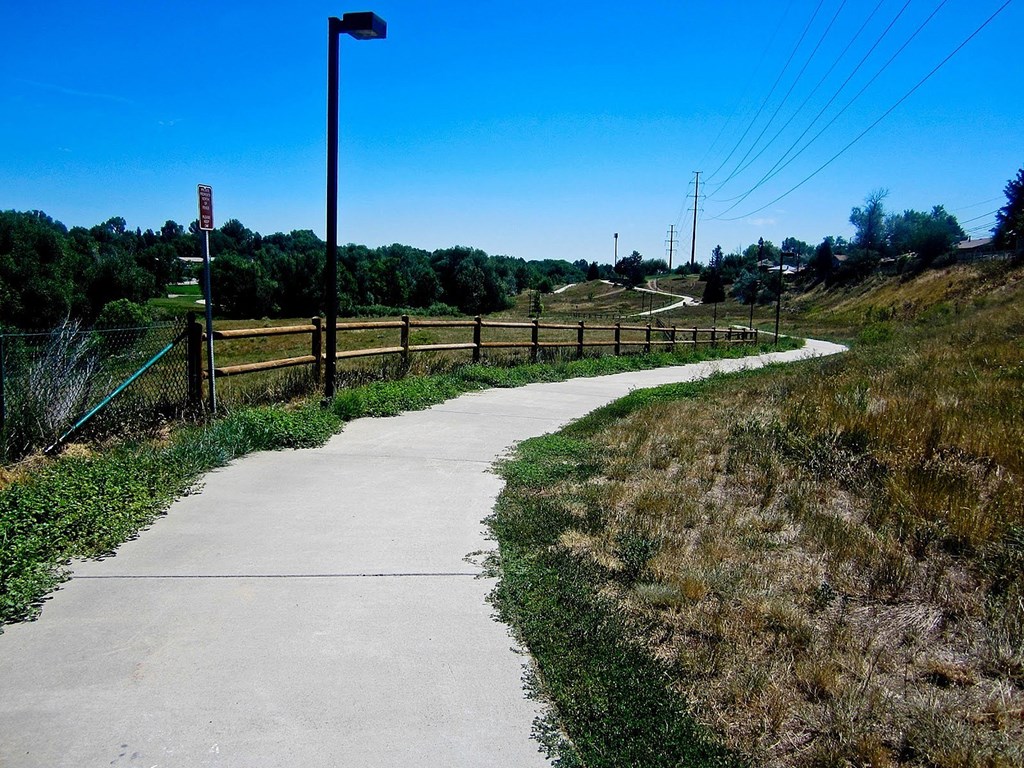 A concrete pathway with a metal fence on one side and a grassy area on the other.