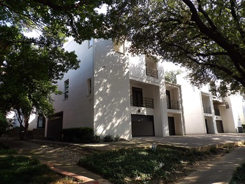 A white building with balconies is surrounded by trees.