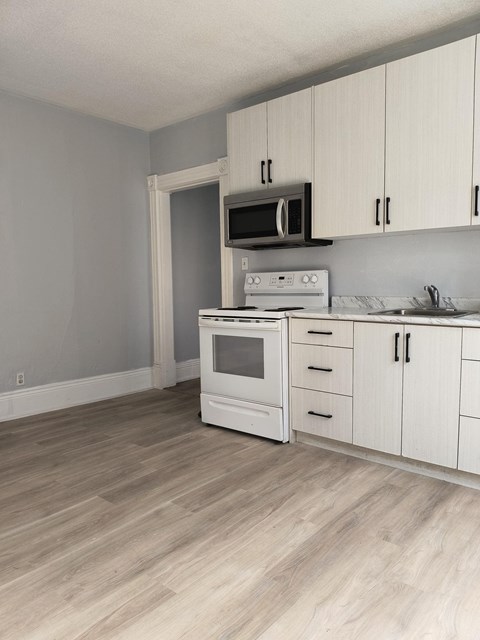 A kitchen with white cabinets and a wood floor.