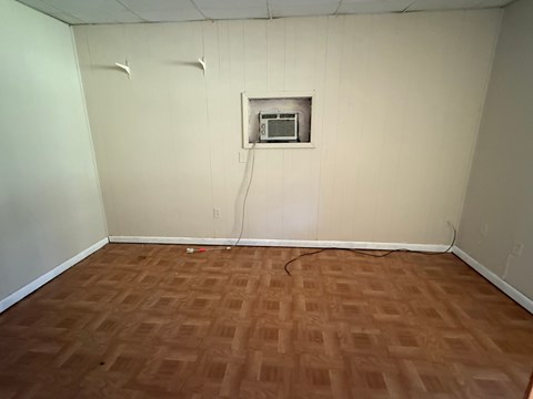 A room with a brown floor and a white wall with a vent.