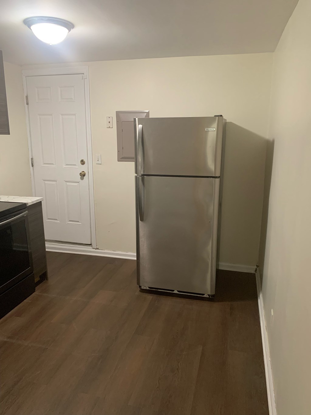 A stainless steel refrigerator sits in a kitchen next to a white door.