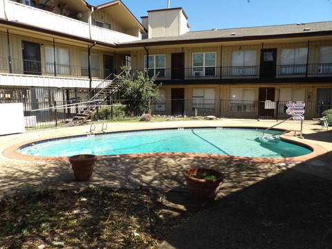 A pool in a courtyard surrounded by potted plants and apartment buildings.