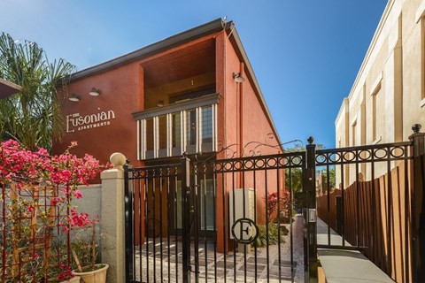 The image shows a red building with a black gate and a sign that reads "Fusionian Apartments".