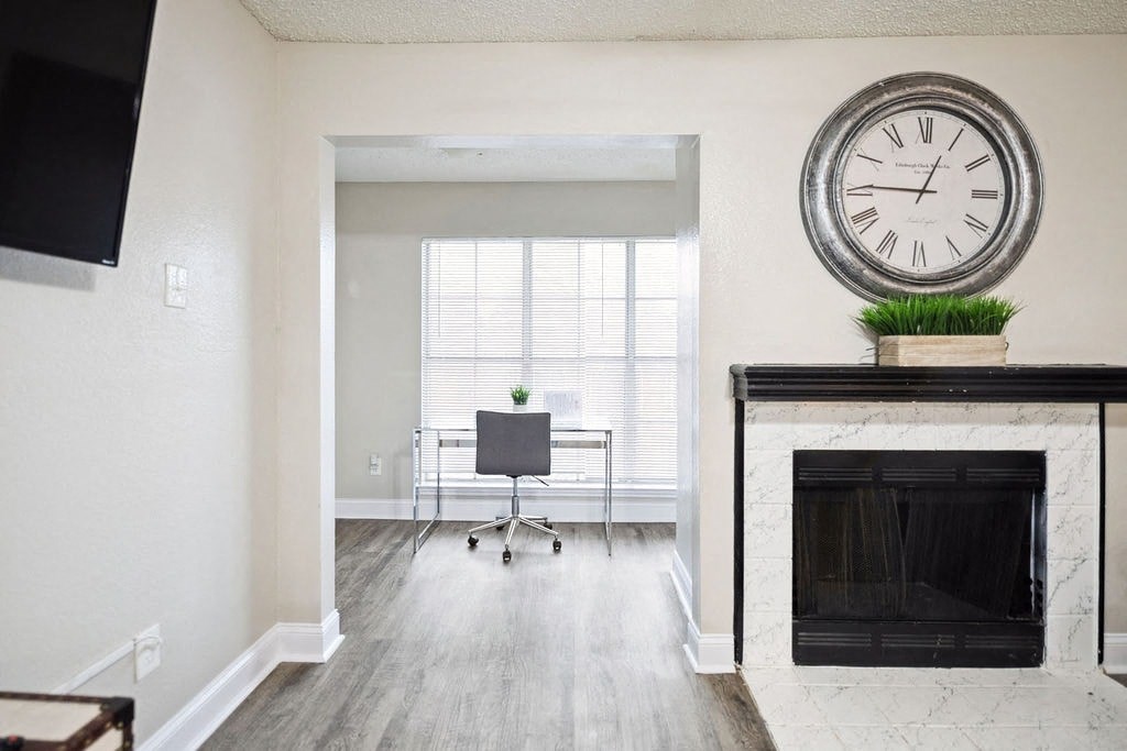 A large clock sits on top of a fireplace in a well-lit room.