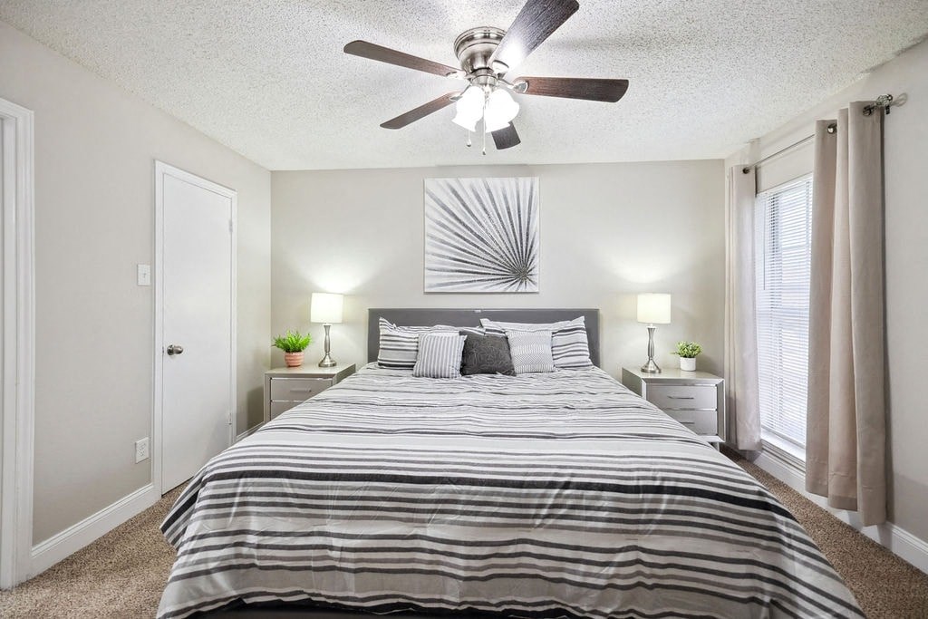 A bedroom with a bed, two lamps, and a ceiling fan.